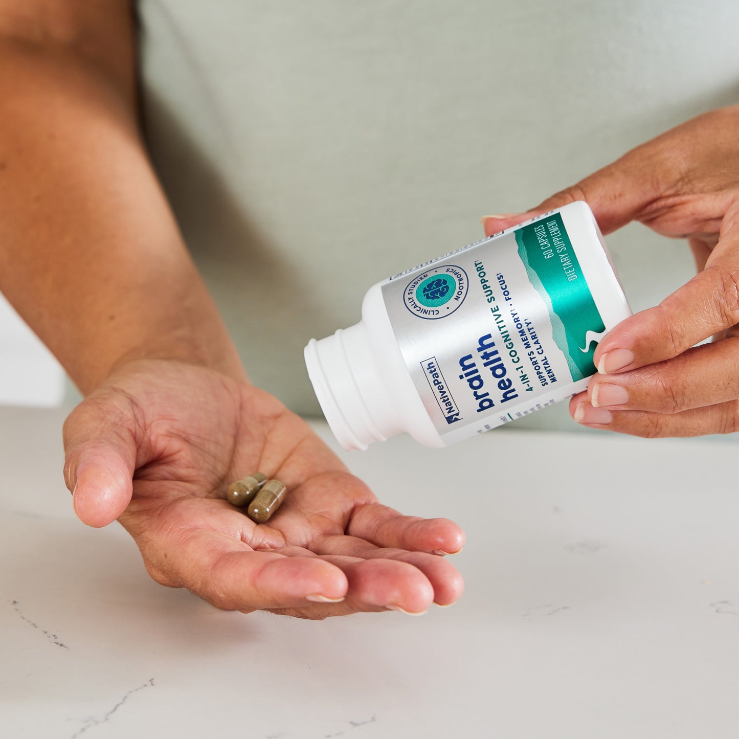 Woman pouring two NativePath Brain Health capsules into her palm from the bottle