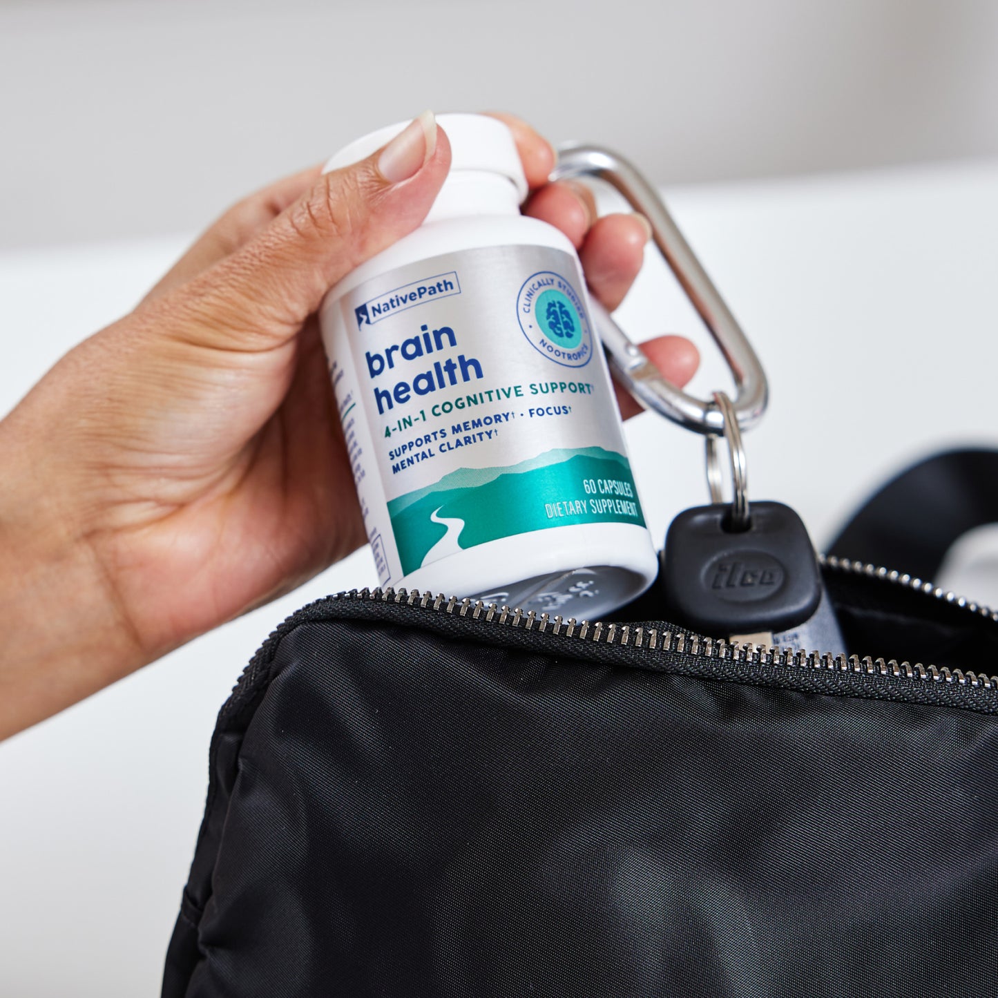 Hand holding a NativePath Brain Health bottle clipped to a bag with a carabiner, showing it's easy to take on the go
