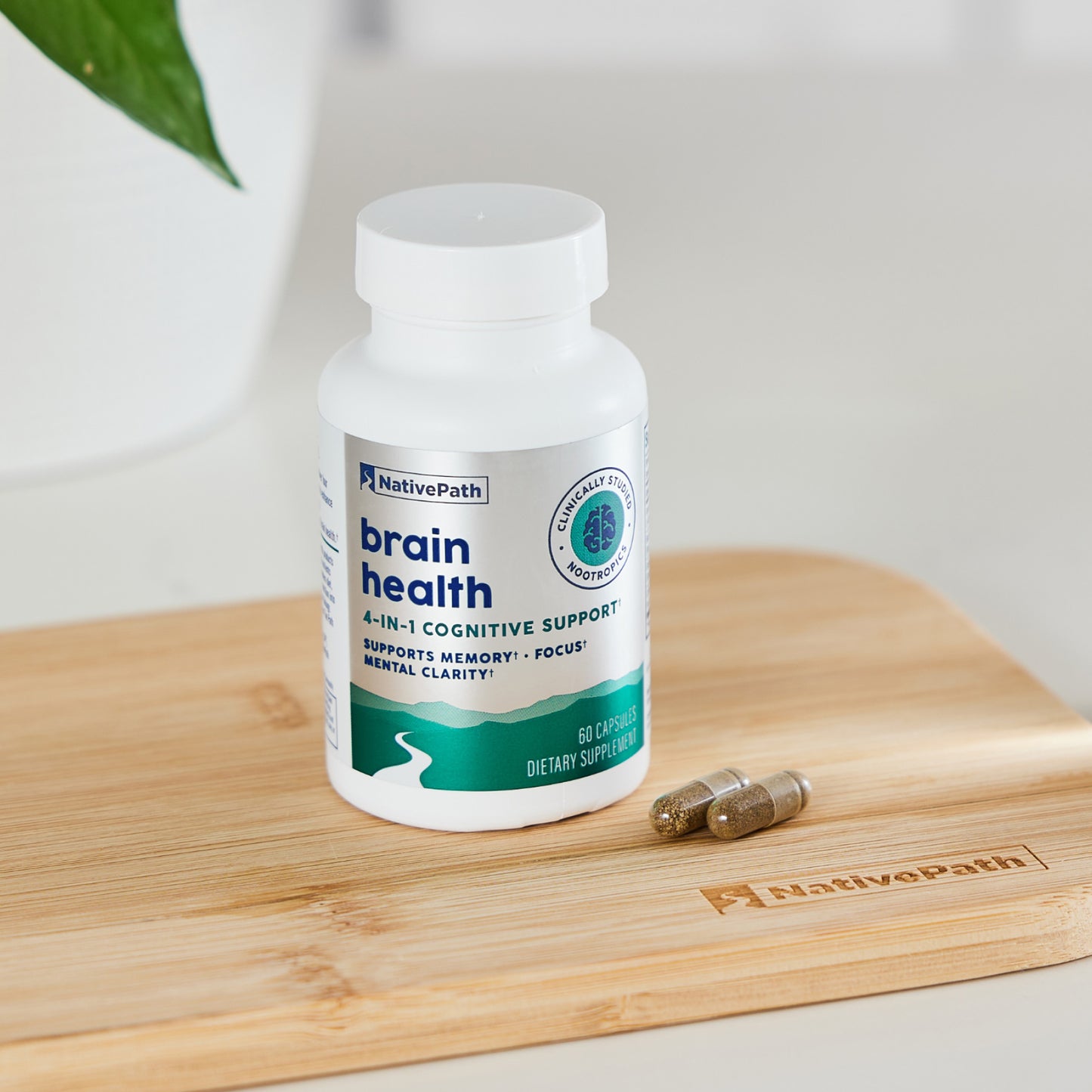 NativePath Brain Health bottle on a wooden cutting board with two capsules and a plant in the background