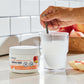 Hand stirring a mixed glass of Native NAC next to the jar, with peaches on the counter