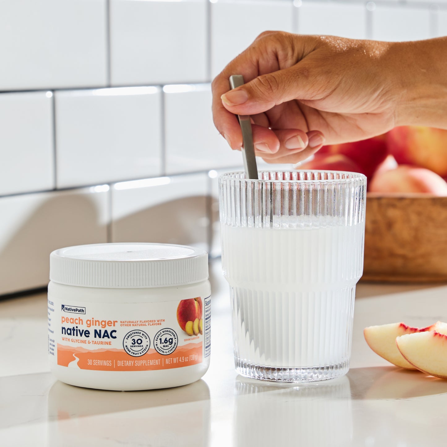 Hand stirring a mixed glass of Native NAC next to the jar, with peaches on the counter